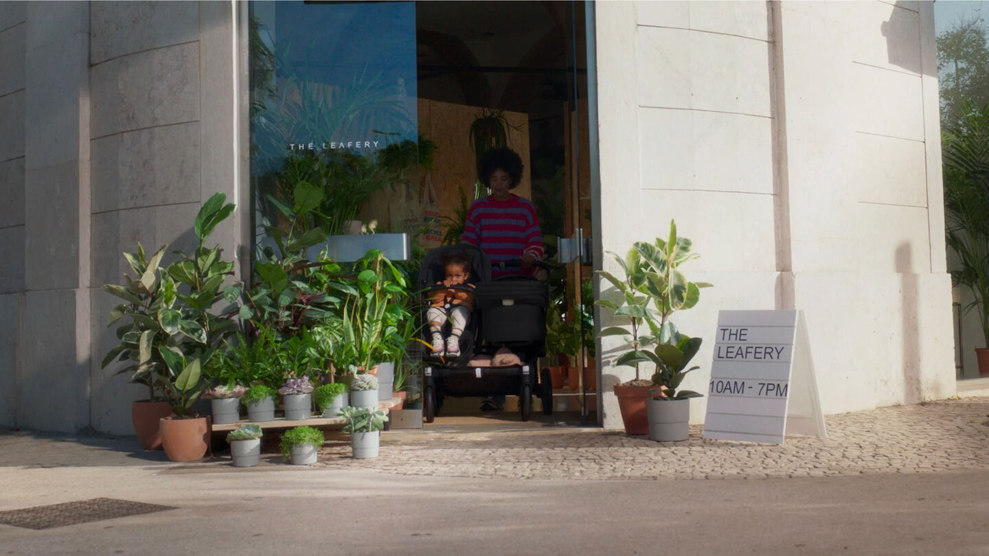 Video: En mamma går ut från ett kafé med sitt barn i en Bugaboo Donkey 5 Duo-vagn. Frodiga växter omger entrén.