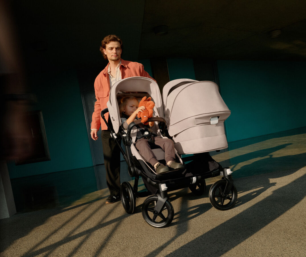 A dad steers his Bugaboo Donkey 5 Duo pushchair at a sharp angle. A toddler sits in the seat of the pushchair.