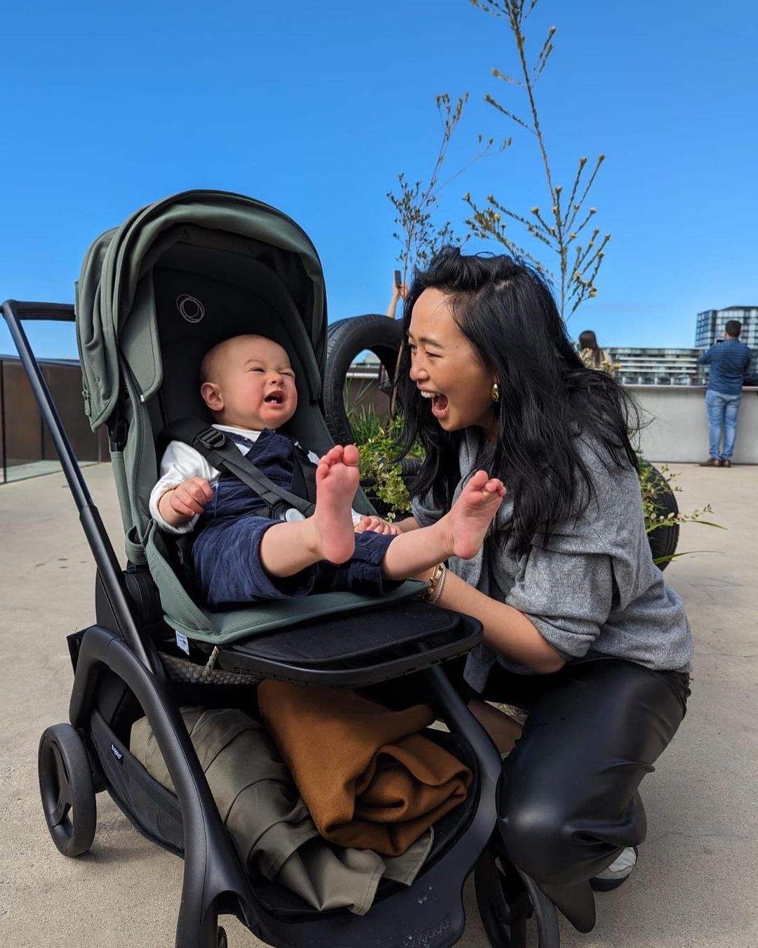 A mom laughs with her baby, who is sitting inside a Bugaboo Dragonfly. The underseat basket is chock full of their items.