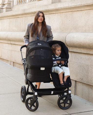 A stylish mom walks with her kids in a Bugaboo Donkey 5. Her daughter sits facing outward, while her baby in the bassinet faces her.