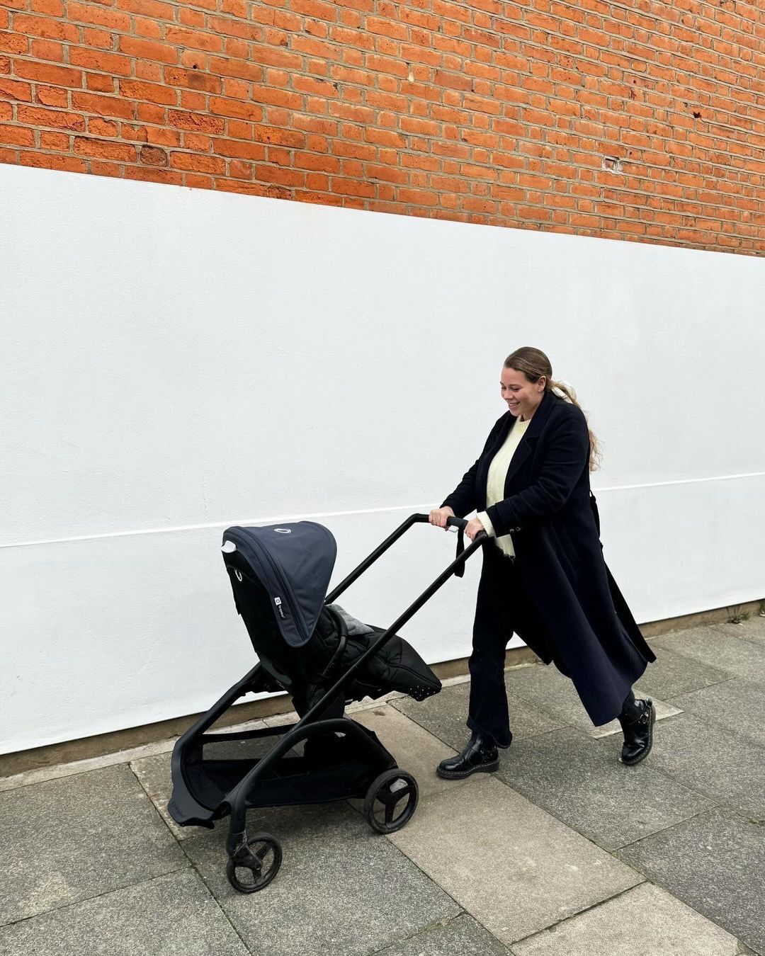 Een vrolijk gestemde moeder wandelt op een trottoir met haar baby in een Bugaboo Dragonfly.