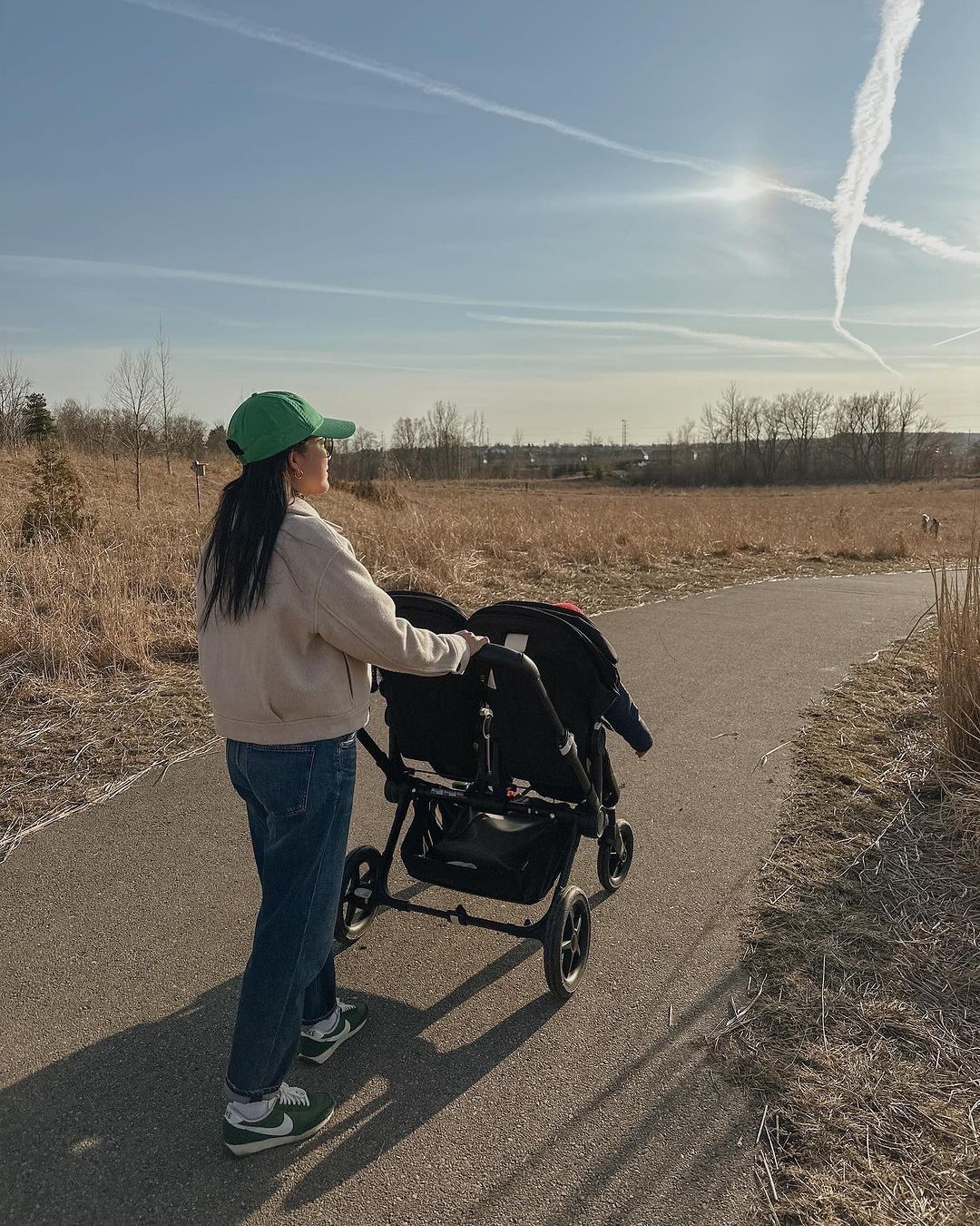 A mom strolls with her kids in a Bugaboo Donkey 5 stroller. They're walking on a paved path in the open countryside.