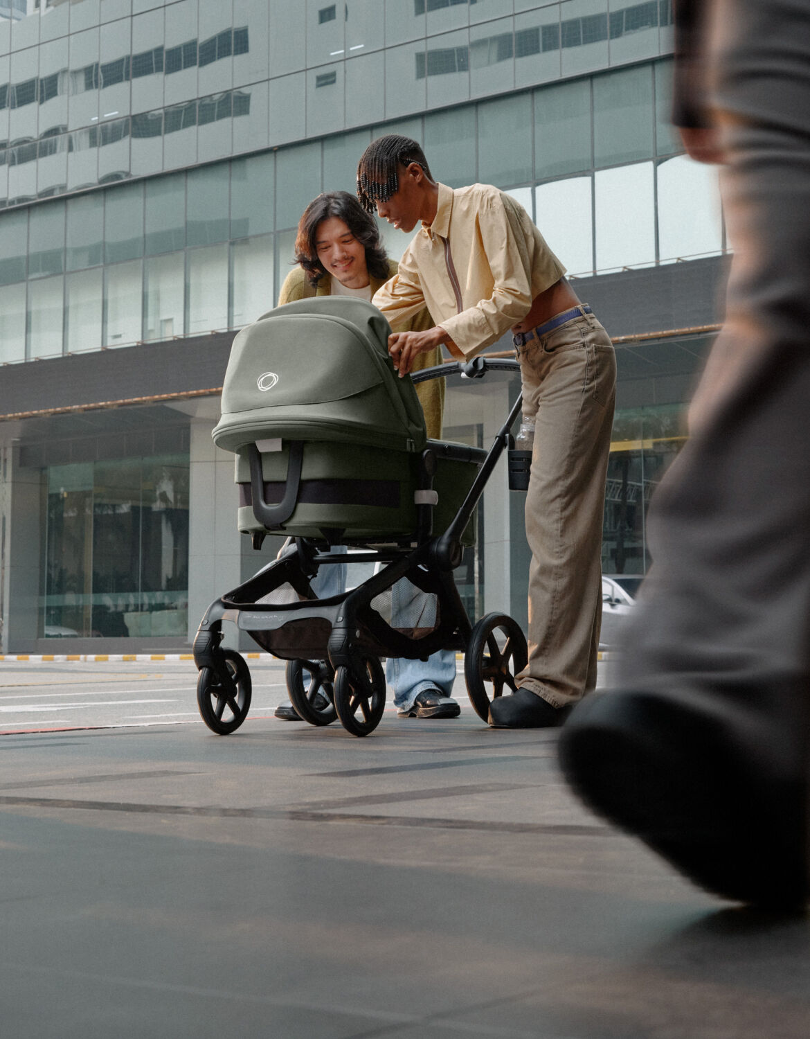 Zwei Eltern stehen mitten auf einer belebten Straße und lächeln ihr Baby an, das in einem Bugaboo Fox 5 Kinderwagen liegt.
