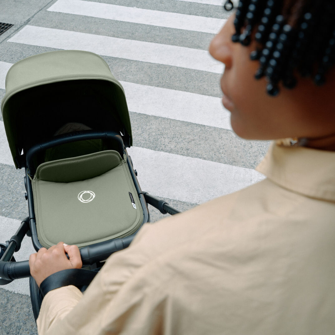 A parent pushing a Bugaboo Fox 5 pushchair with one hand.
