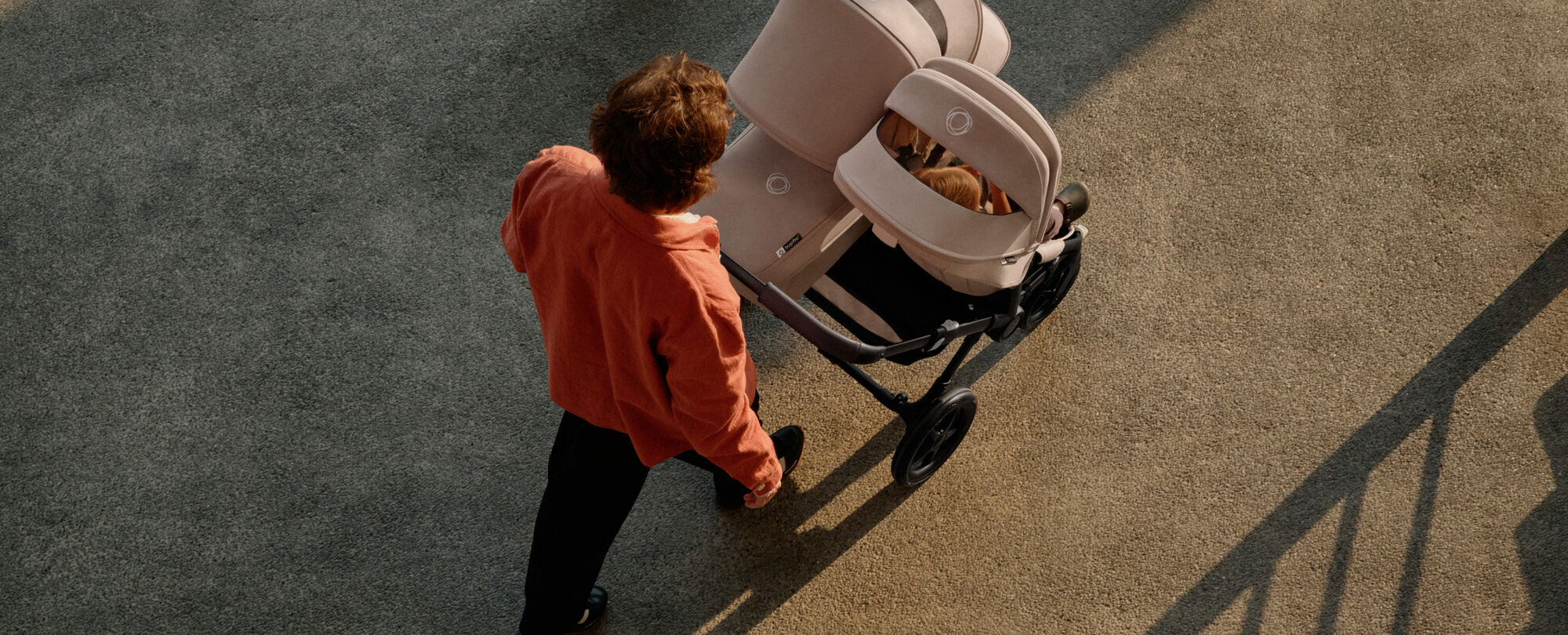 Bird eye's view of a dad walking with a Bugaboo Donkey 5 Duo. The pushchair has a seat and a bassinet, in Desert Taupe colourway.